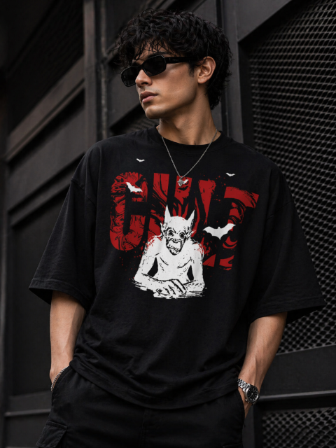 Man wearing a black t-shirt with a graphic design against a dark textured wall.